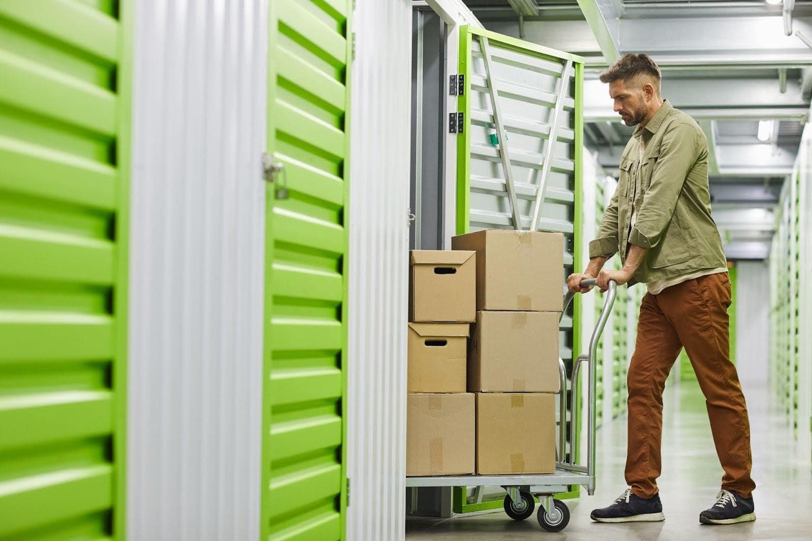 A man pushes a cart filled with boxes in a cluttered storage room