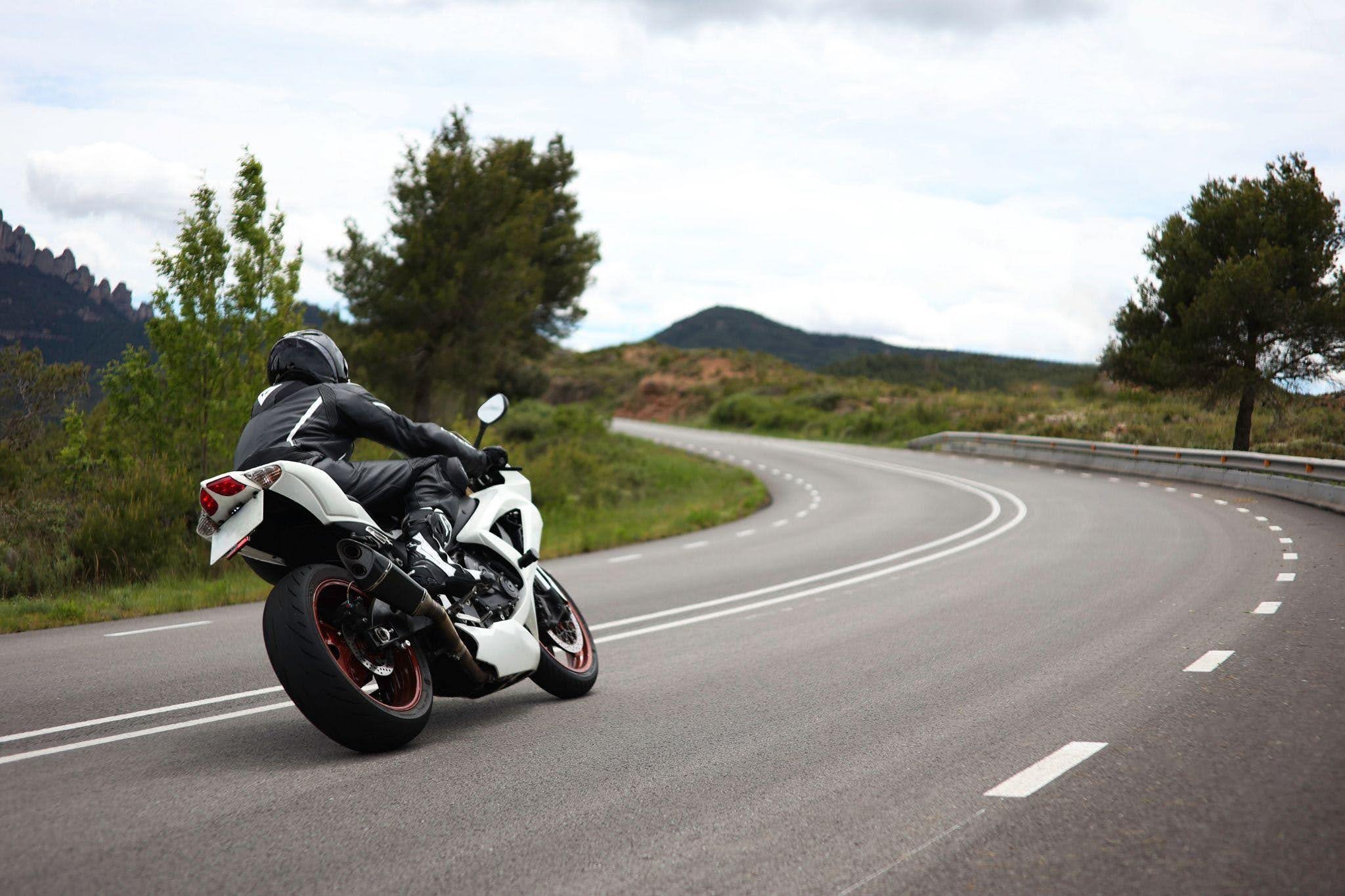A person riding a motorcycle along a winding road surrounded by trees and hills